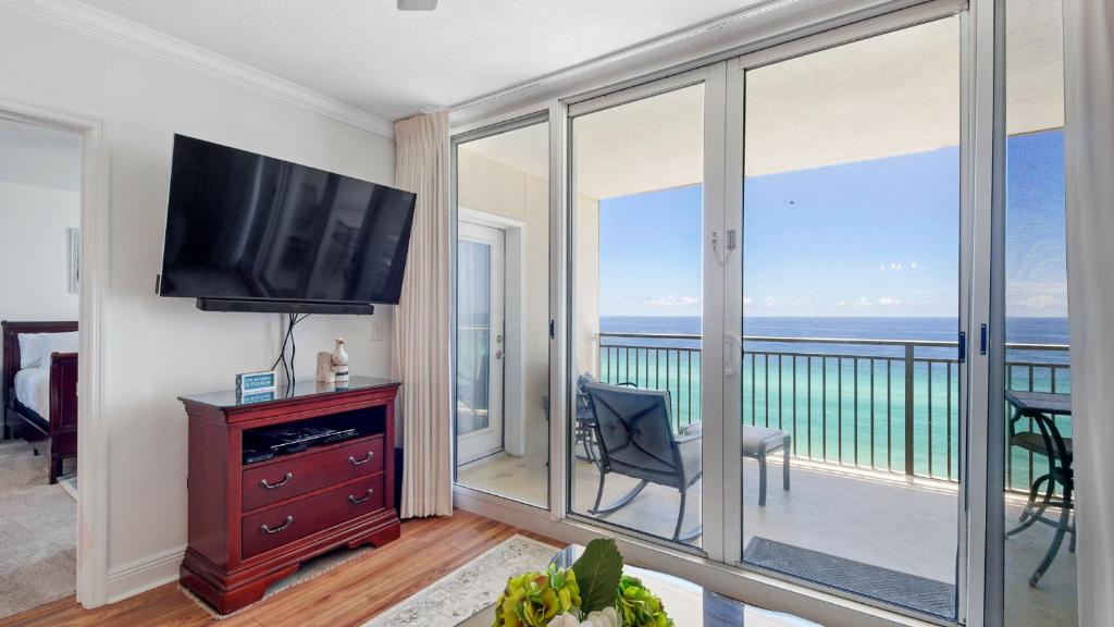 a living room with a television and a balcony with the ocean at Emerald Beach #1331 by Nautical Properties Vacation Rentals in Panama City Beach