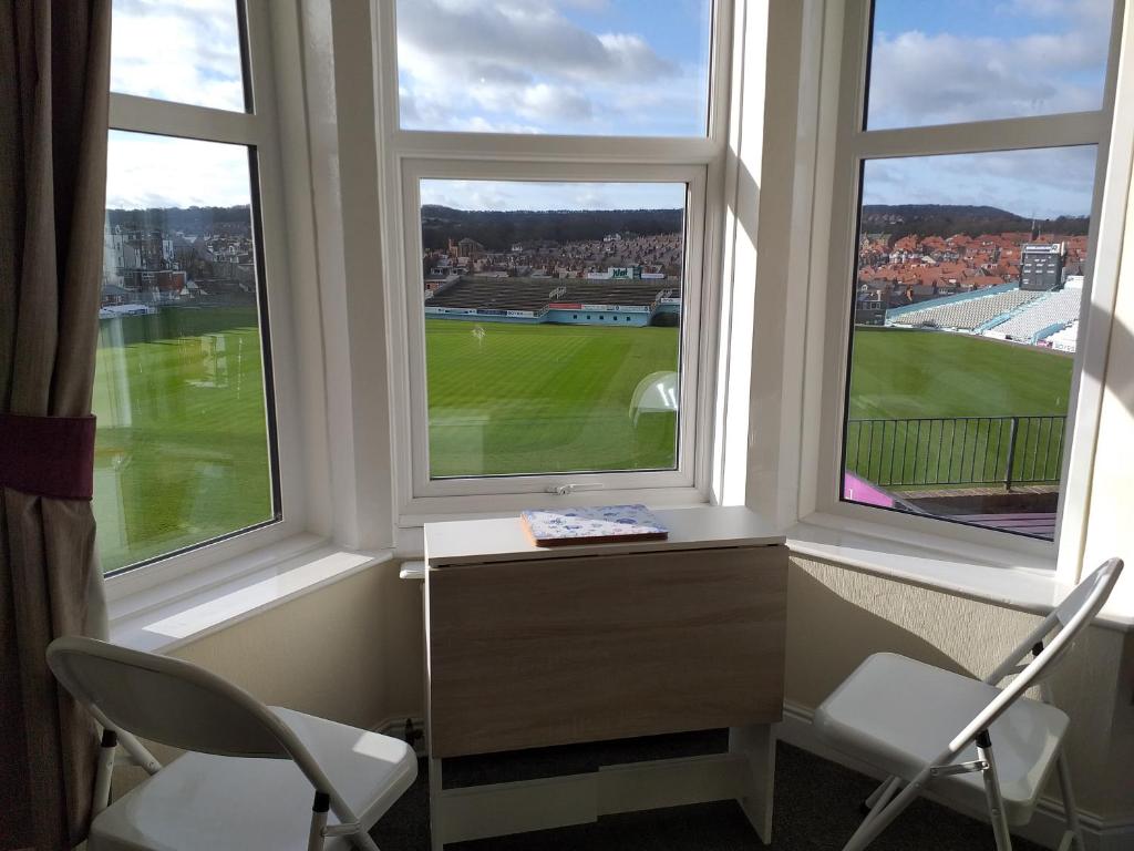 een kamer met 2 stoelen, een bureau en 2 ramen bij Cricket Stadium View in Scarborough