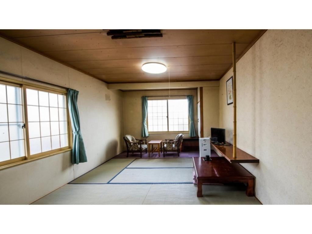 uma sala de estar com uma mesa, cadeiras e janelas em Onsen Hotel Tsutsujiso - Vacation STAY 03255v em Kitami