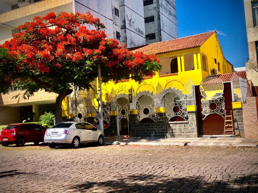 a yellow building with a tree with red flowers at Dom Alberto Hostel in Corumbá