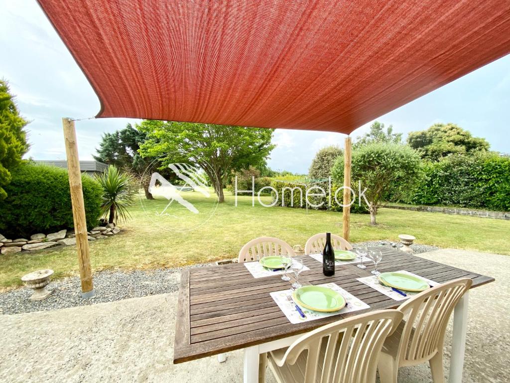 einen Holztisch mit Stühlen unter einem roten Regenschirm in der Unterkunft Jolie maison récente confort Proche des plages in Riantec