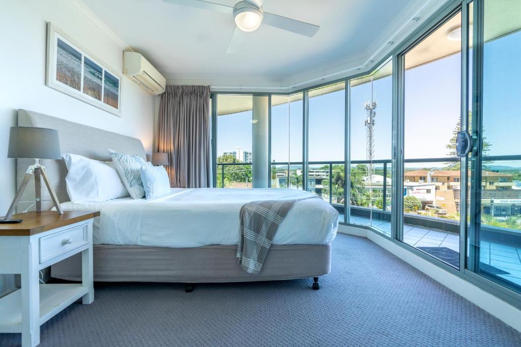 a bedroom with a bed and a balcony with windows at Sails Apartments in Forster