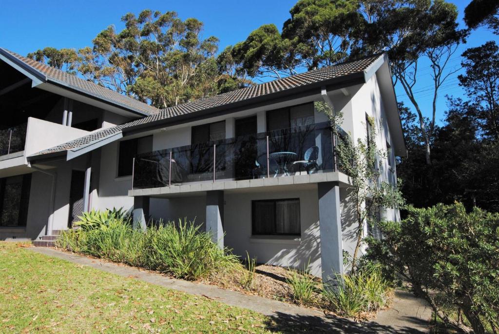 a white house with a balcony and trees at Beachfront Unit - Belle Escapes Jervis Bay in Vincentia