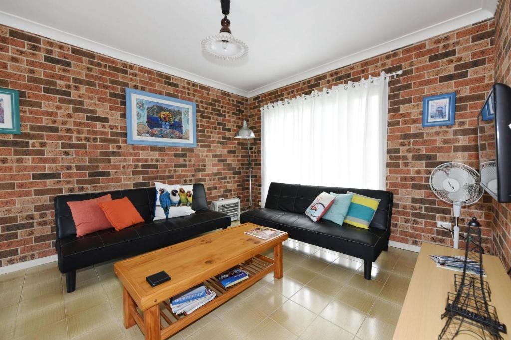 a living room with a black couch and a brick wall at Excellent Location - Belle Escapes Jervis Bay in Vincentia