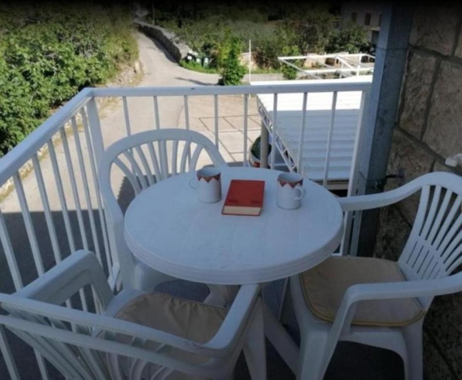 einen Tisch mit 2 Stühlen und ein Buch auf dem Balkon in der Unterkunft Apartment Antea - private parking & garden in Čilipi