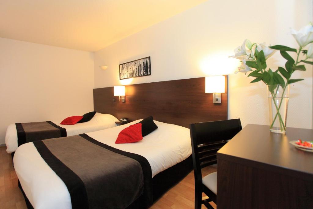 a hotel room with two beds and a table and flowers at Hôtel Castellane in Toulouse