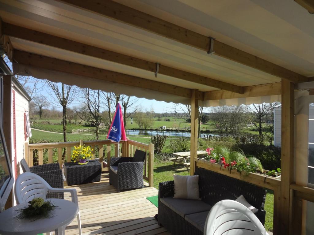a wooden pergola with a couch and chairs on a deck at Normandie 3 chambres Plages débarquement Mobile home in Litteau