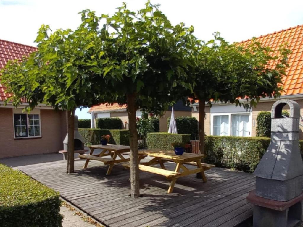 un patio con 2 mesas de picnic y un árbol en De Friese Antillen en Hollum
