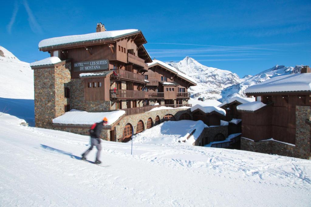 Un uomo sta sciando su una pista innevata di fronte a un edificio di Hôtel Les Suites du Montana by Les Etincelles a Tignes
