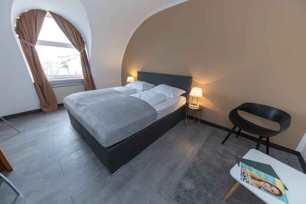 een slaapkamer met een bed, een stoel en een raam bij Skycity Hotel Atrigon in Klagenfurt