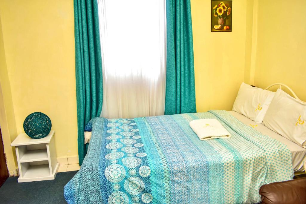 a bedroom with a bed with a blue blanket and a window at Classic Studio Milimani - Wi-Fi and Parking in Kisumu