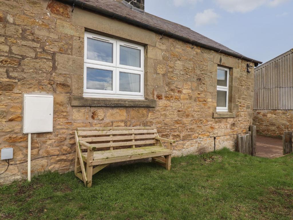 a wooden bench sitting outside of a brick building at Pond Cottage in Alnwick