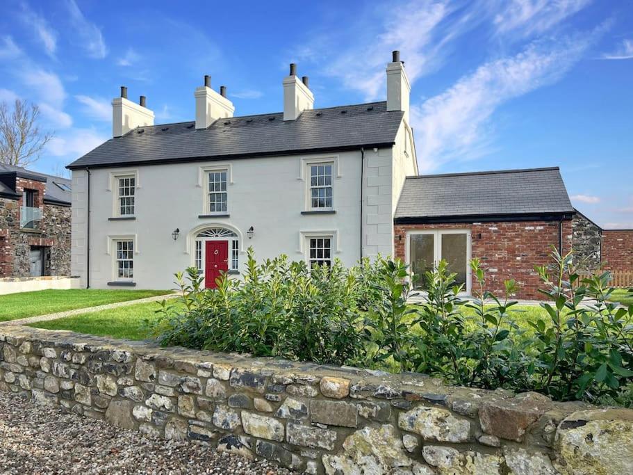 una casa bianca con una porta rossa e un muro di pietra di The Farmhouse at Corrstown Village a Portrush
