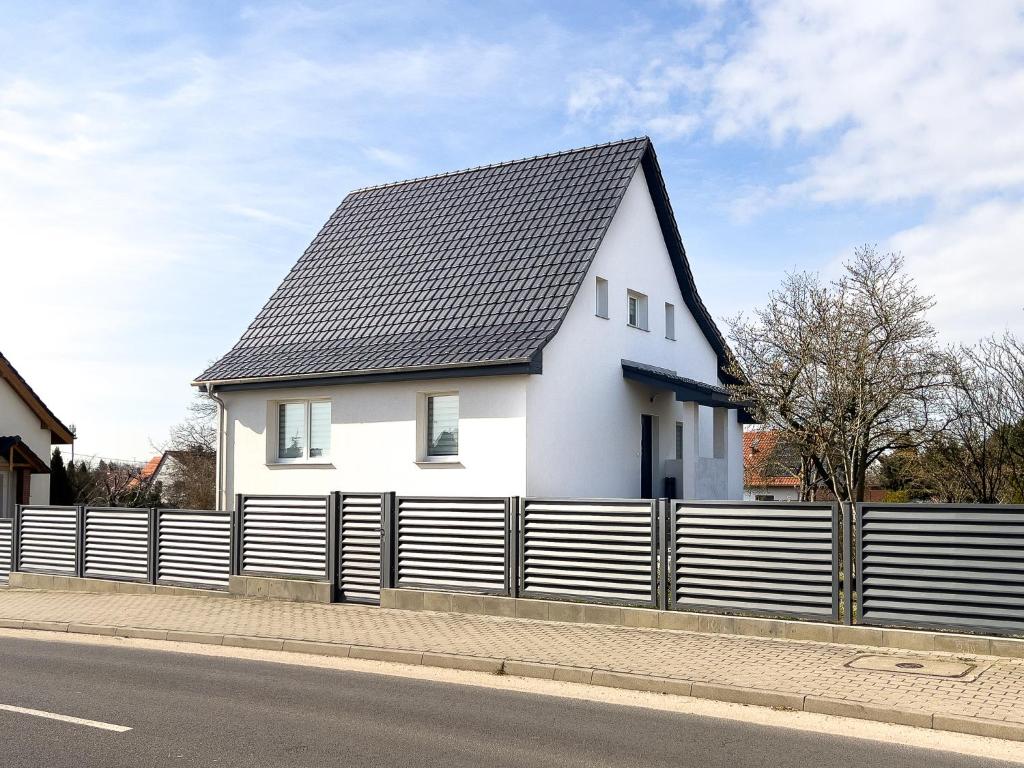 a white house with a black roof behind a fence at Noclegi Krańcowa in Zgorzelec