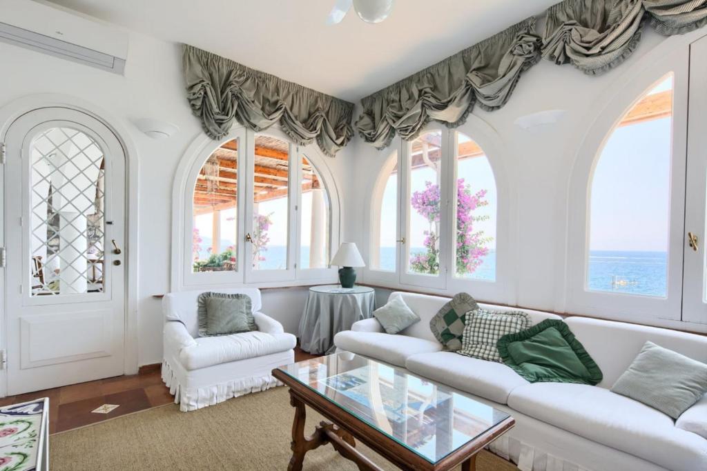 una sala de estar con muebles y ventanas blancos. en Estate4home - Villa San Montano, en Massa Lubrense