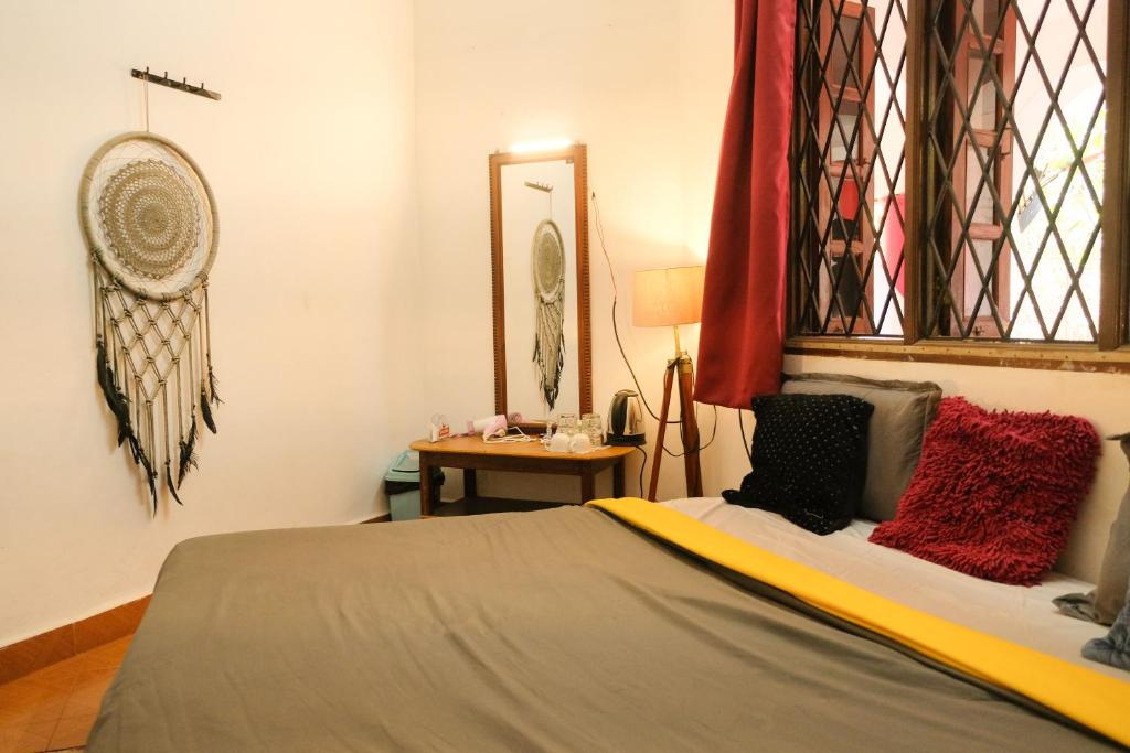 Schlafzimmer mit einem Bett mit roten Kissen und einem Spiegel in der Unterkunft Mitra Hostel Vagator in Vagator