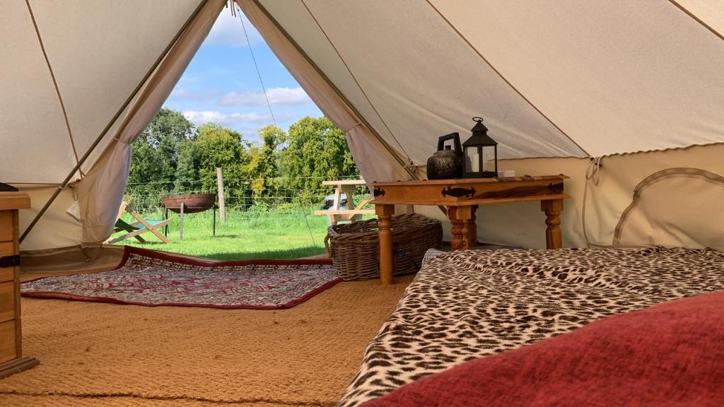 a tent with a bed and a table and a field at Home Farm Radnage Glamping Bell Tent 5, with Log Burner and Fire Pit in High Wycombe