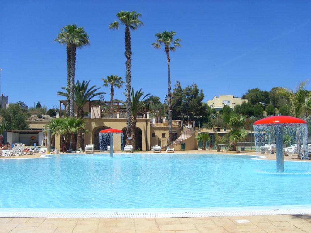 a large swimming pool with palm trees in the background at Sporting Club Village in Mazara del Vallo