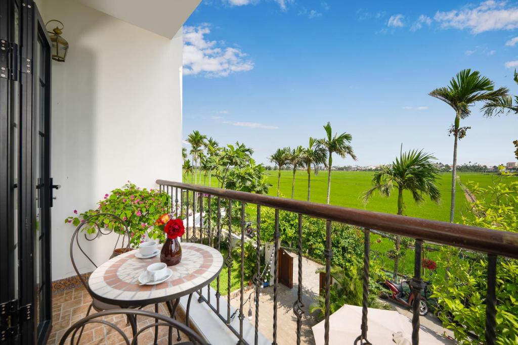 een balkon met een tafel en uitzicht op een veld bij Maison Fleur Luxury Hoi An in Hội An