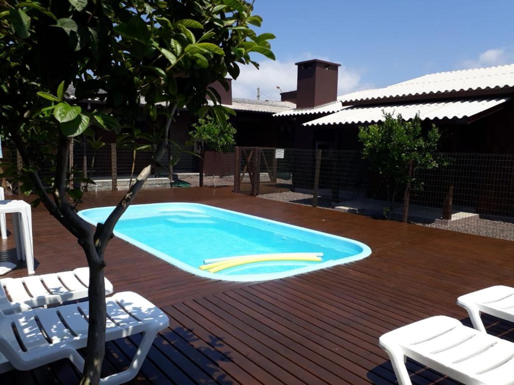 a swimming pool with two lawn chairs and a tree at Lindo Residencial na Praia Itapeva Torres in Torres