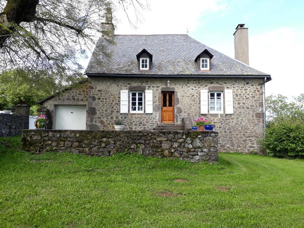 a stone house with a stone fence in front of it at Gîte du Bosquet Pays de Salers Cantal in Sainte-Eulalie