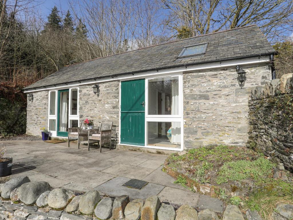a stone cottage with a green door and a patio at Llo Bach Bach in Abergele