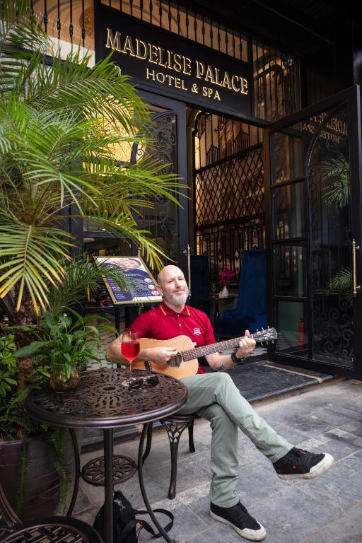 a man sitting in a chair playing a guitar at Madelise Palace Hotel & Travel in Hanoi
