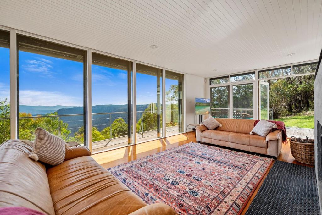 Escarpment Hideaway في Medlow Bath: غرفة معيشة مع كنب ونوافذ كبيرة