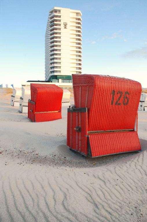 three red chairs on a beach with a building in the background at Hotel Neptun in Warnemünde