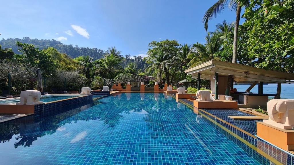 einen Pool in einem Resort mit Stühlen und dem Meer in der Unterkunft Baan Khaolak Beach Resort in Khao Lak