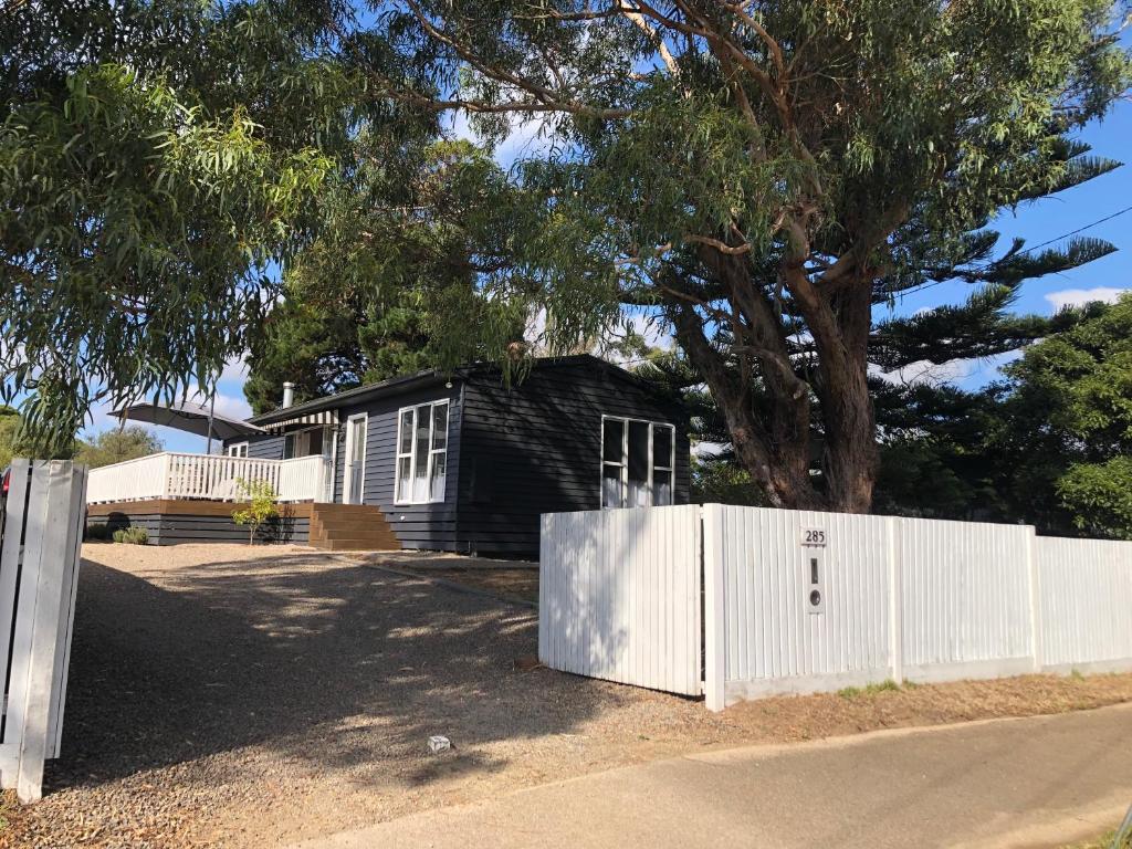 a black house with a white fence and a tree at Jetty Road Beach House in Rosebud