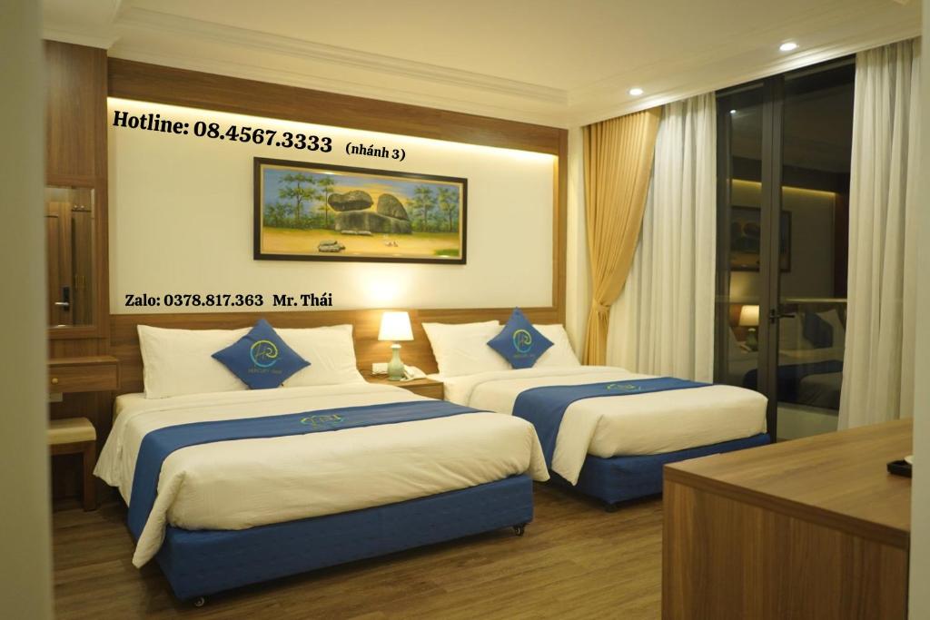 a hotel room with two beds with blue and white sheets at Khách sạn Hercury FLC Sầm Sơn in Sầm Sơn