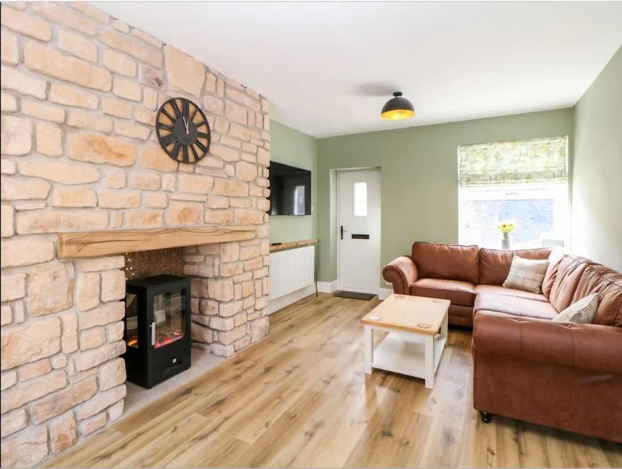 a living room with a couch and a stone fireplace at Babbling Brook Cottage in Stony Middleton