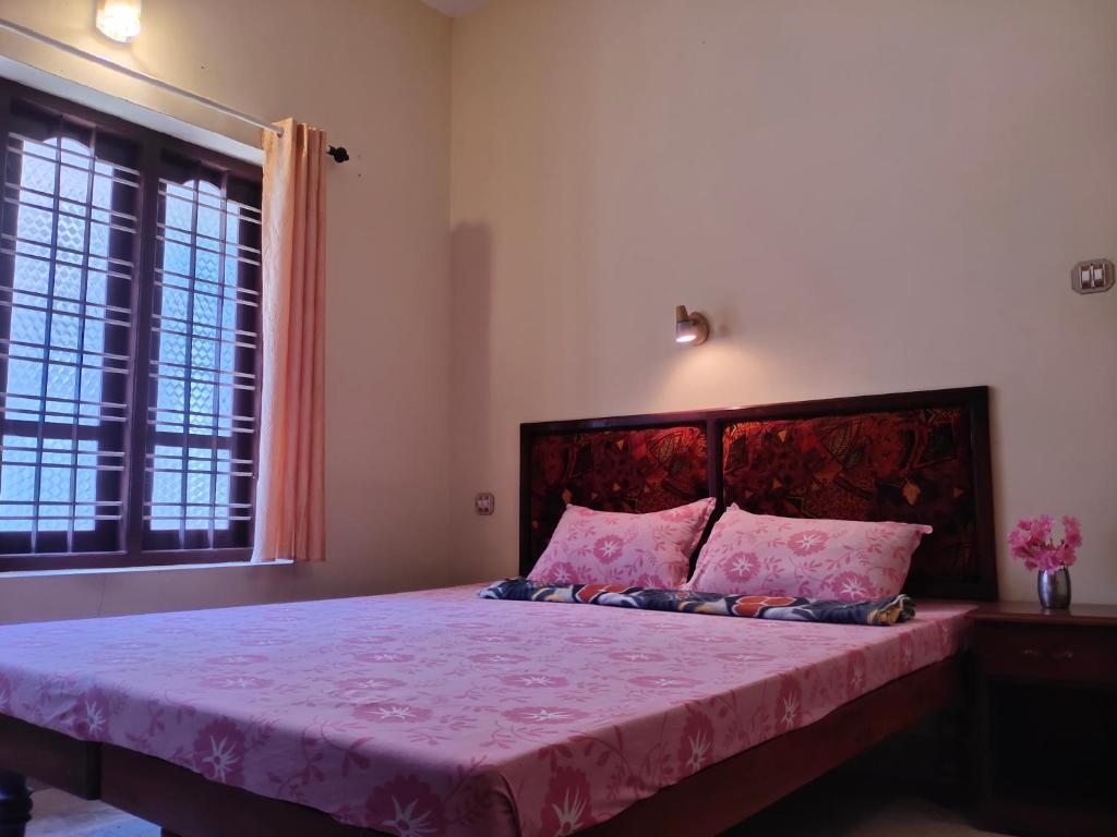 1 dormitorio con cama con sábanas rosas y ventana en PALAZHI, en Kovalam