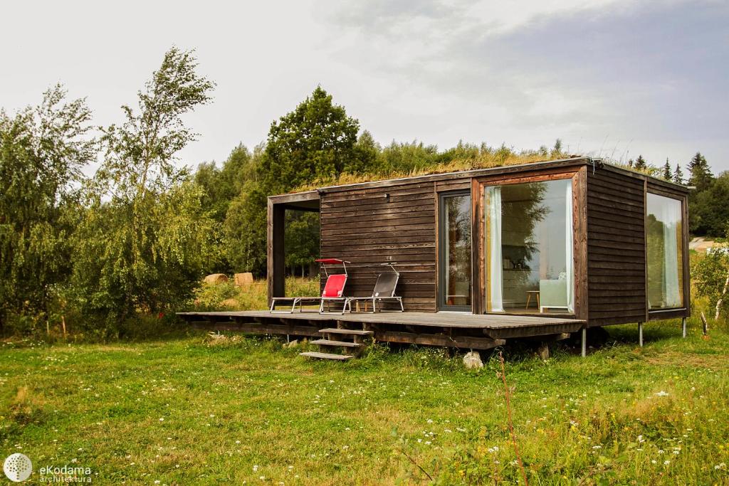 a small wooden cabin with two chairs on a field at BioDomek, naturalny dom z przepięknymi widokami na góry in Gniewoszów