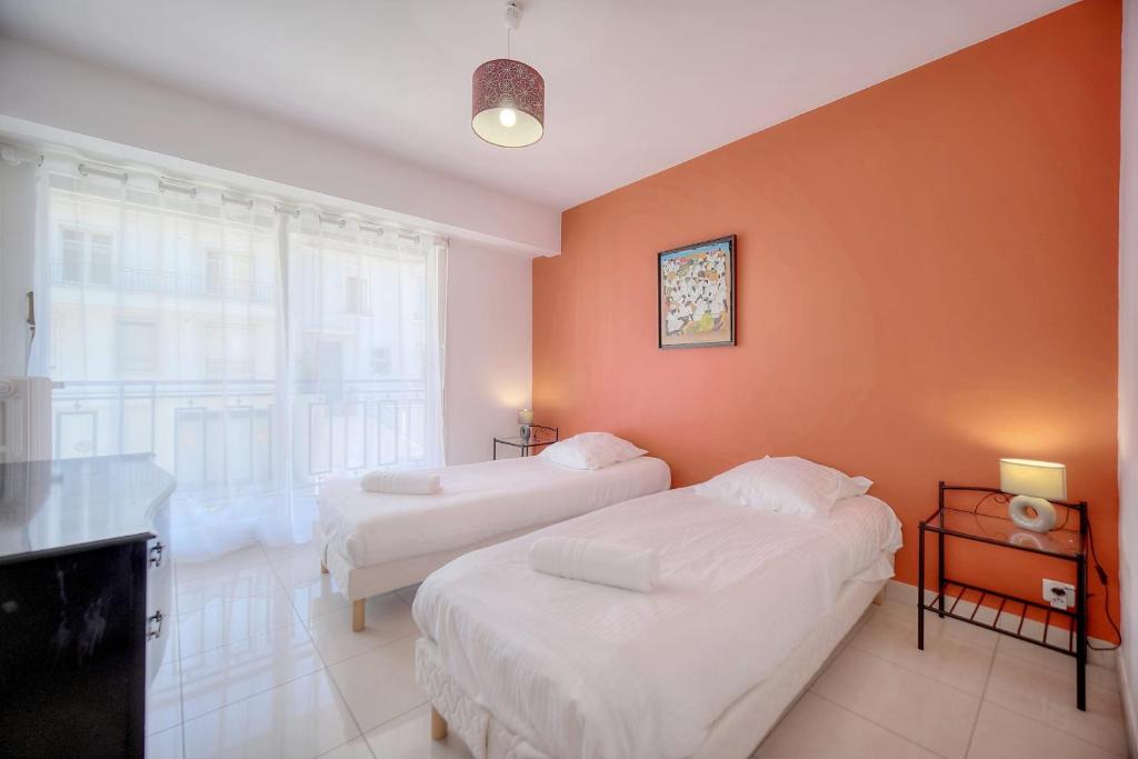 two beds in a room with an orange wall at IMMOGROOM - Renovated apartment - Terrace - AC in Cannes