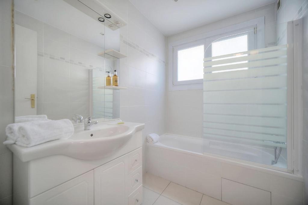 a white bathroom with a sink and a tub and a window at IMMOGROOM - Renovated apartment - Terrace - AC in Cannes