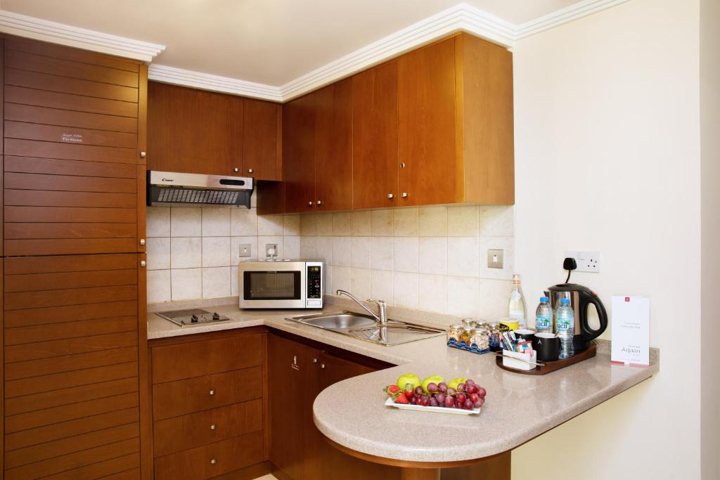 a kitchen with wooden cabinets and a bowl of fruit on a counter at Al Rawda Arjaan by Rotana, Abu Dhabi in Abu Dhabi