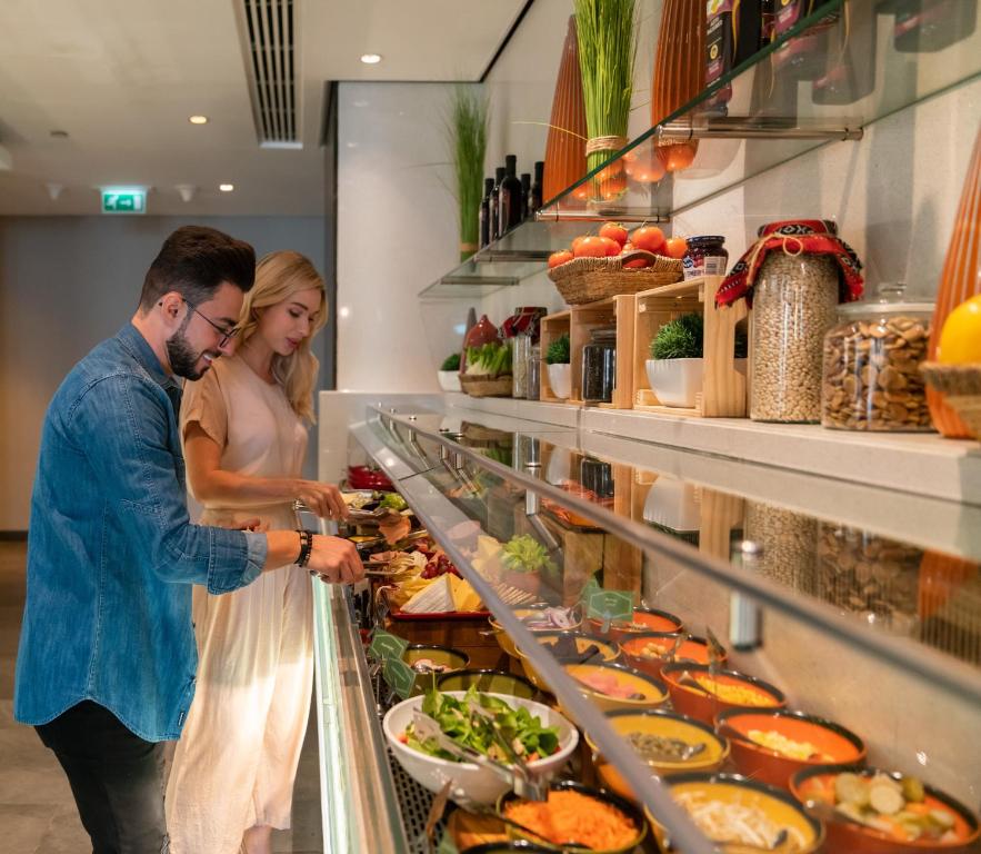 a man and a woman looking at food in a buffet at Centro Al Manhal by Rotana in Abu Dhabi
