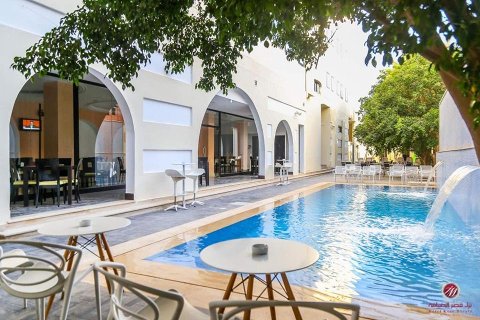 - une piscine avec des tables et des chaises à côté d'un bâtiment dans l'établissement Hotel KSAR DHIAFA by PLAZA HOTELS & RESORTS, à Sidi Bouzid