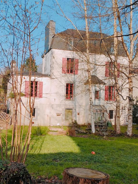 une vieille maison blanche avec des fenêtres rouges et une souche d'arbre dans l'établissement Ty Merzhin, à Huelgoat