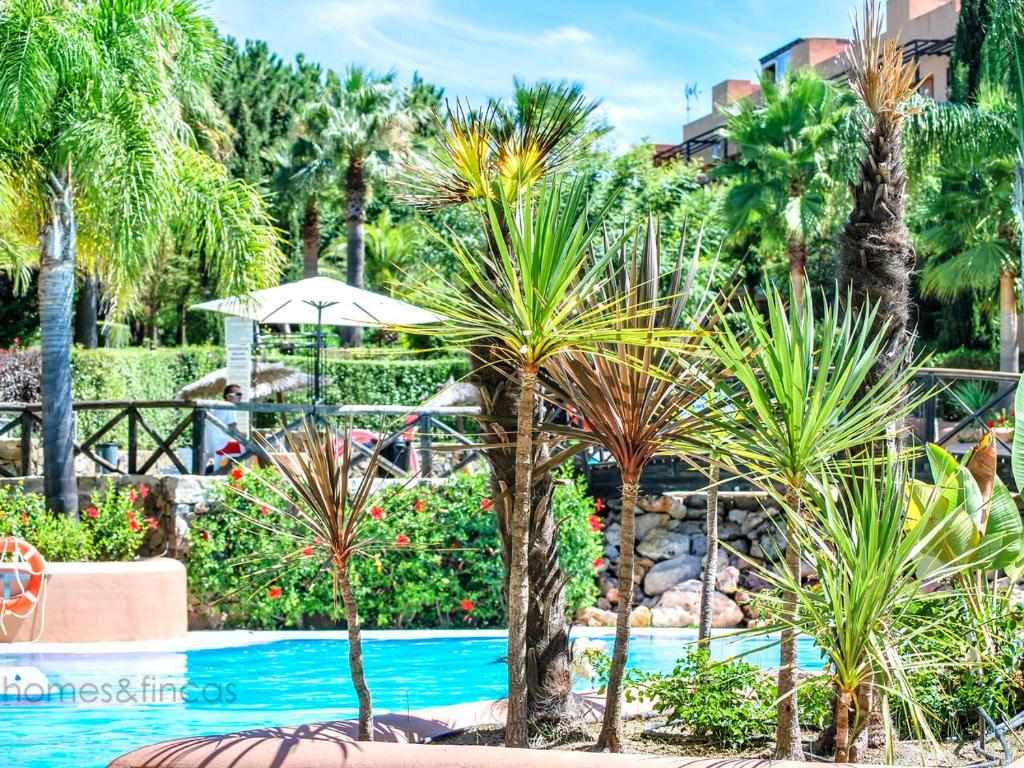 uma piscina de resort com palmeiras e um guarda-sol em Beautiful 3 Bed Townhouse in Islantilla Golf em Islantilla
