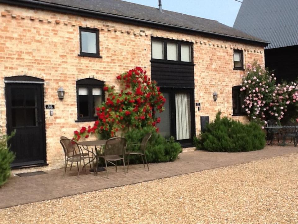 uma casa de tijolos com mesa, cadeiras e flores em Rural Farm Cottage Easy Commute To Cambridge em Cambridge