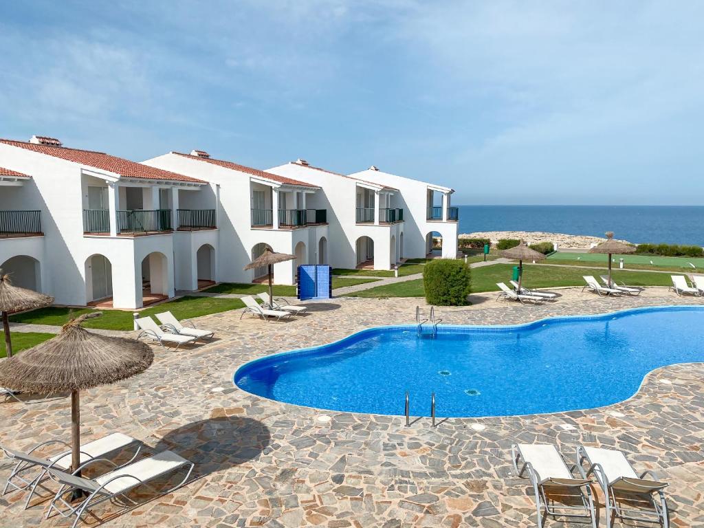 a villa with a swimming pool in front of the ocean at RVHotels Sea Club Menorca in Cala en Blanes