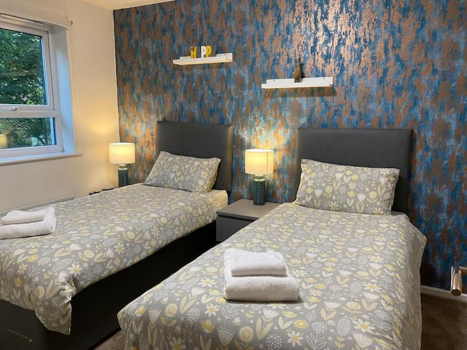 two beds in a bedroom with blue wallpaper at Cheerful 4-bedroom house with multiple car parking in Manchester