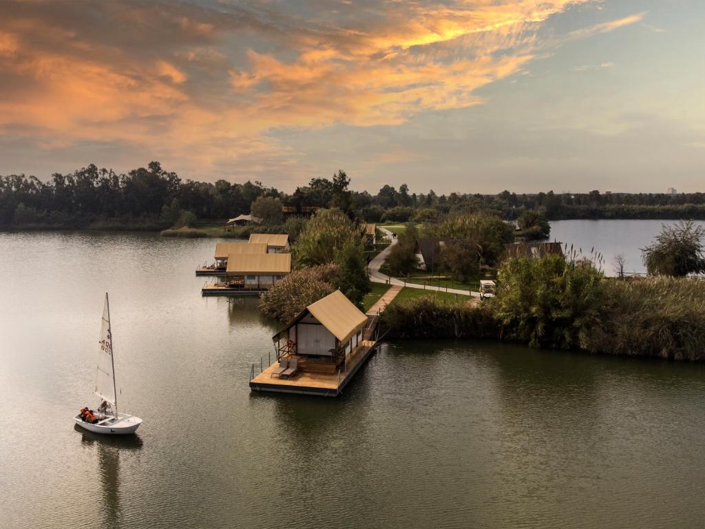 a boat on a lake with a house and a sailboat at Nabi Resort Glamping & SPA in Castel Volturno