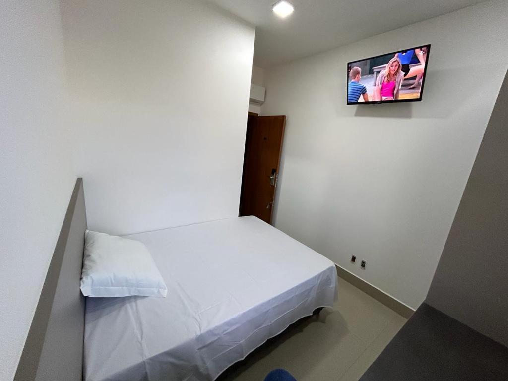 Habitación pequeña con cama y TV en la pared. en NANO Suítes, en Uberlândia