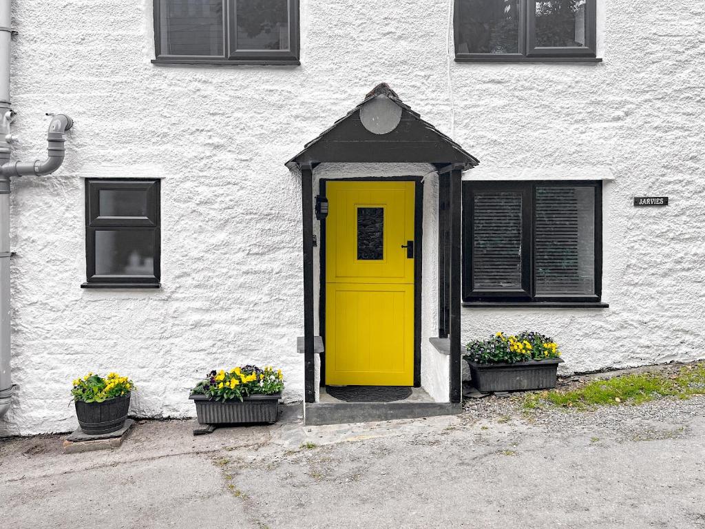 a yellow door on a white building with two plants at Jarvies Cottage in Boscastle