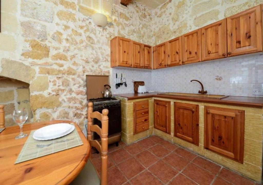 cocina con armarios de madera, mesa y fogones en Tan-Nahla (128B) Holiday Farmhouse with Private Pool en Il-Pergla