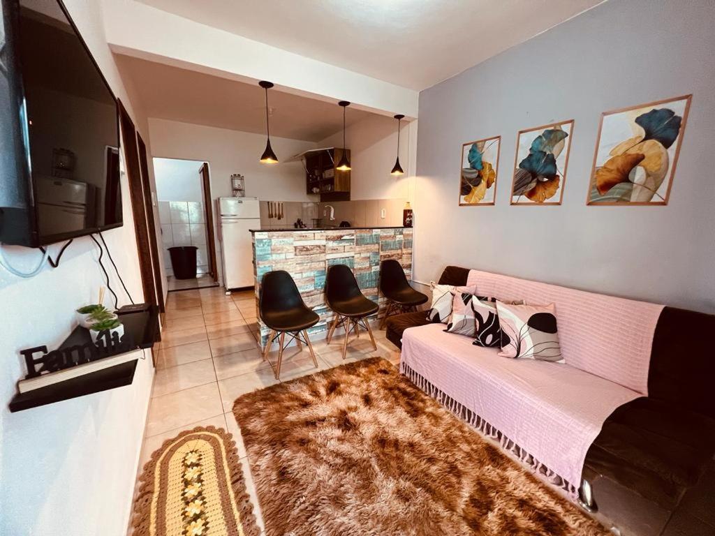 uma sala de estar com um sofá rosa e cadeiras em Apto Aconchego da Aldeia próximo ao centro e praias em São Pedro da Aldeia
